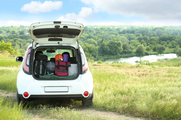 Car with camping equipment in trunk on green field. Space for text © New Africa