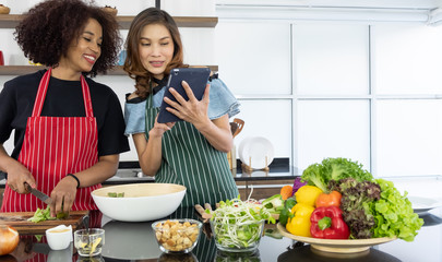 Happy young woman friends different races in apron make salad together 