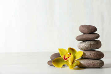 Stack of spa stones and flower on table against white background, space for text