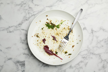 Dirty plate with food leftovers, herbs and fork on marble background, top view