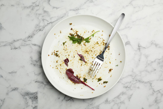 Dirty plate with food leftovers, herbs and fork on marble background, top view
