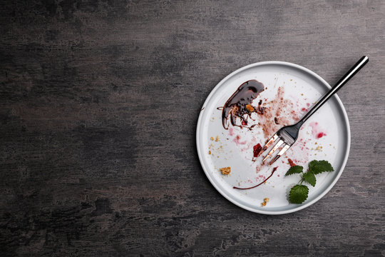 Dirty plate with food leftovers, mint and fork on grey background, top view. Space for text