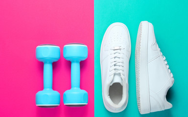 White sneakers, plastic dumbbells on a two-color background. Sport concept. Top view