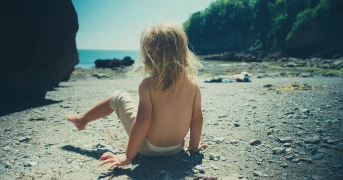 Little toddler sitting on the beach on a sunny summer day