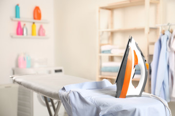 Modern electric iron and clean shirt on board in laundry room. Space for text
