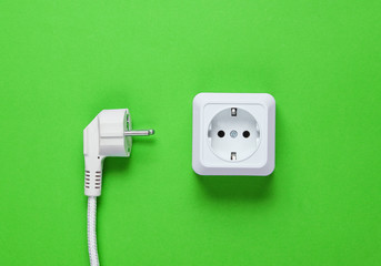 White plastic power socket and power plug on green background. Top view