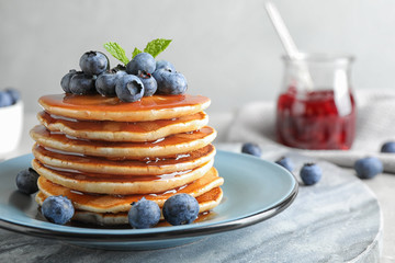 Plate of delicious pancakes with fresh blueberries and syrup on grey table against light background - obrazy, fototapety, plakaty
