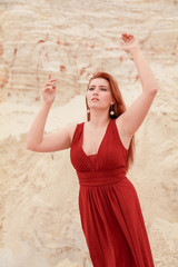 Young beautiful plus size Caucasian woman in red long chiffon dress posing in desert landscape with...