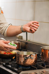 Close-up image of chef preparing food, adding green pease into cooker on a stove.