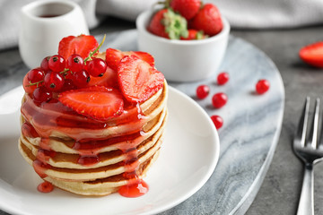 Delicious pancakes with fresh berries and syrup on grey table