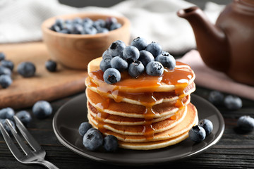 Delicious pancakes with fresh blueberries and caramel syrup on black wooden table