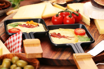 Delicious traditional Swiss melted raclette cheese on diced boiled or baked potato and baguette served in individual skillets with salami..