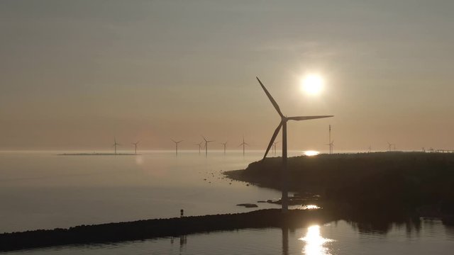 Sunset and windmills. Golden sky and horizon. Rotating mills. Drone shot of landscape with sea. Reflection in the water.