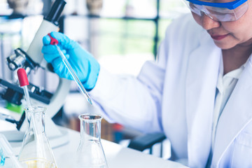 Women scientist looking through microscope in laboratory. Women scientist doing some research with dropper chemical testing.