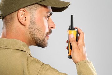 Male security guard in uniform using portable radio transmitter on grey background, closeup