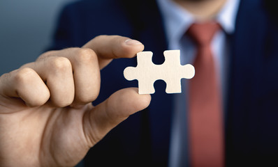 Businessman standing on gray background holds a piece of the puzzle in his hand