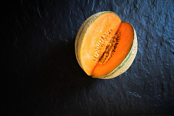 Small, cut melon lying on a stone slab. View from above.