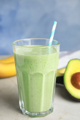 Glass of tasty smoothie and avocado on light grey table