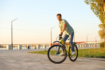 Handsome young man riding bicycle on city waterfront