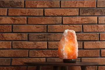 Himalayan salt lamp on table against  brick wall. Space for text