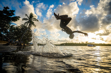 Scenic sunset view of tropical beach scene with unrecognizable silhouette splashing in the waves in...