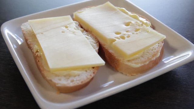 2 white bread sandwiches with butter and cheese on a plate. the camera moves around this to the left. close-up