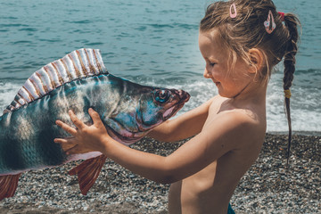 little girl on the beach with big fish - obrazy, fototapety, plakaty