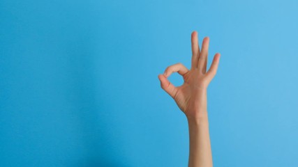 Female hand showing ok gesture over blue background. Body language concept.