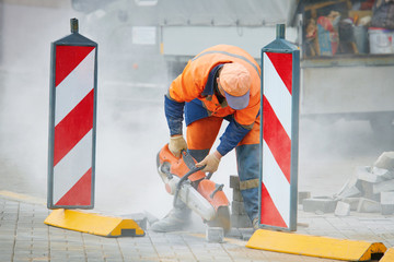 Worker in uniform cut concrete brick with circular saw. Repairing and renewal the walkway. Builder,...