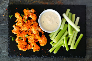 Cauliflower buffalo wings with celery and ranch dip. Top view on a slate serving platter. Healthy...