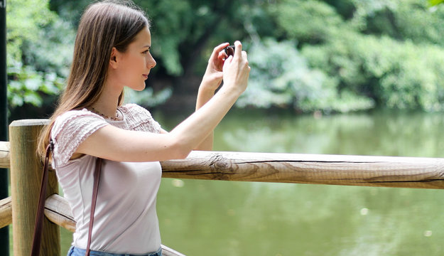 Young woman using her smartphone outdoor in a park and taking pictures