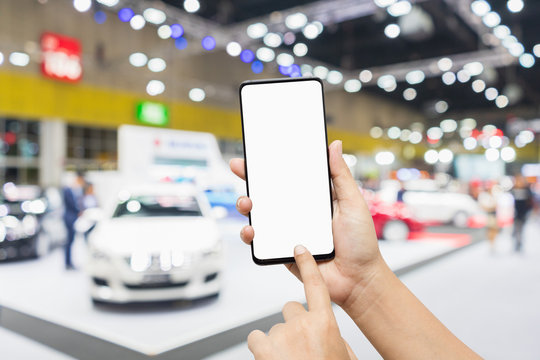 Mock up mobile phone. Hand holding smartphone with abstract Blurred defocused image of public event exhibition hall showing cars and automobiles. Mockup mobilephone for your advertisement.