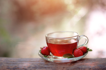Fruit red tea with wild berries in glass cup, in forest, on bright background.