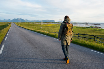 Man with backpack walking on an empty road. Amazing landscape, mountain and ocean. Scenic view. New way. Enjoy the moment, relaxation. Wanderlust. Travel, adventure, lifestyle. Explore North Norway
