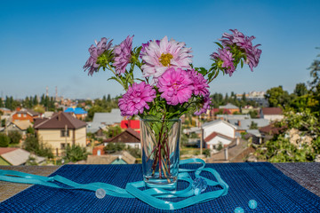 Fototapeta na wymiar summer, day, blue, sky, distance, houses, buildings, window sill, blue, background, small, glass, vase, plants, pink, chrysanthemums, small, flowers, asters, bouquet, narrow, silver, ribbon, round, wh