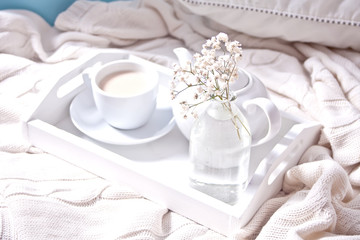 Close up of cup of tea, milk, teapot and bouquet of white flowers on the white tray.