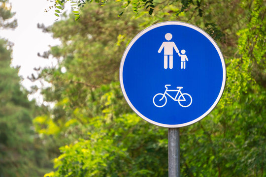 Blue bicycle lane and pedestrians sign on green trees background