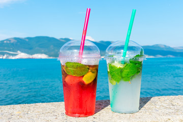 Summer cooling drinks. Two mojitos on the beach. Close up. Red and green cocktails on blue sea background. Refreshments