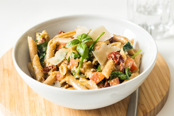 Whole wheat pasta with fresh and dried tomatoes, basil and parmesan cheese in white bowl