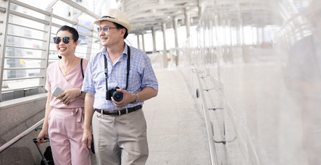 Senior Asian couple with a woman dragging a suitcase and talking happily with smiling at the...