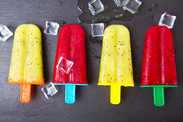 Homemade popsicle with lime juice, kiwi fruit and raspberry against black stone background.