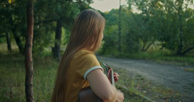 beutiful young woman in yellow shirt on nature background in forest sitting ,  playing on her guitar and smiling , look at the camera with emotions