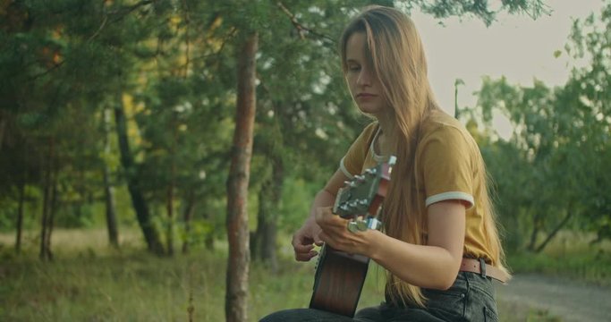 beutiful young woman in yellow shirt on nature background in forest sitting ,  playing on her guitar and smiling , look at the camera with emotions