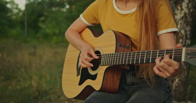 beutiful young woman in yellow shirt on nature background in forest sitting ,  playing on her guitar and smiling , look at the camera with emotions