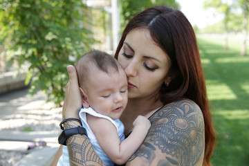 Portrait Happy young mother kisses her cute newborn baby. Happy family, motherhood, parenting, people and childcare concept. In the park.