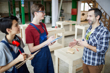 Side view portrait of mature carpenter teaching group of trainees holding clipboards in joinery...