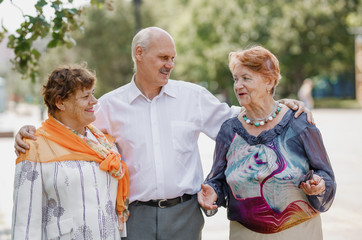 Old man and two old women are happily walking together in a park on a warm day