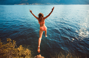 Young woman jumping from a rock into the sea.