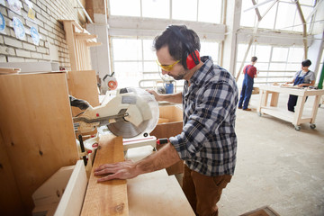Fototapeta na wymiar Side view waist up portrait of mature carpenter sawing wood in industrial workshop, copy space