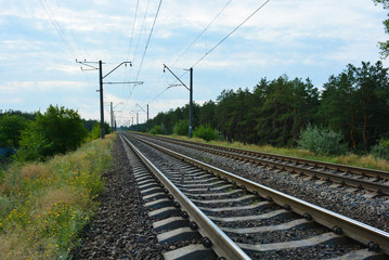 Railway track, railway and electric power lines for electric vehicles, electric trains lying along coniferous forests with blue sky, clouds. Infrastructure of Severny housing estate, Dnipro, Ukraine.